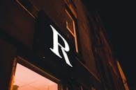 Close-up of an illuminated storefront sign with the letter "R" against a dark night sky.